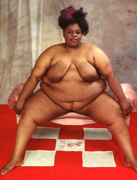 Fiatal kövér néger nő meztelenül ücsörög a kanapén lógó melleivel